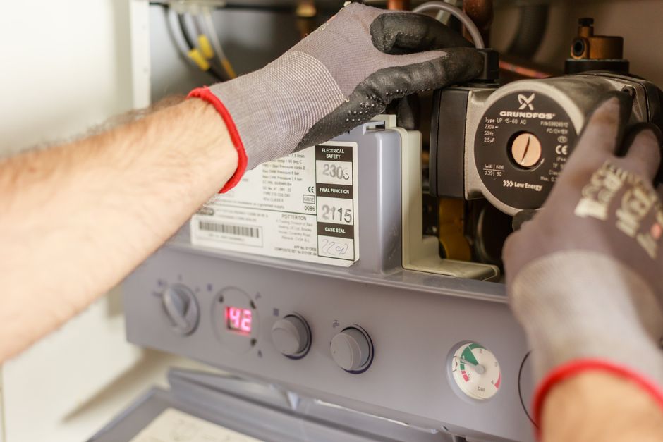 A plumber’s hands adjusting the controls of a boiler system with pressure gauges